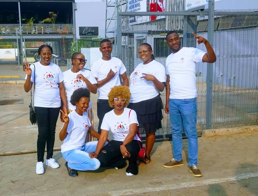 Group of people wearing matching white t-shirts posing for a photo outside.