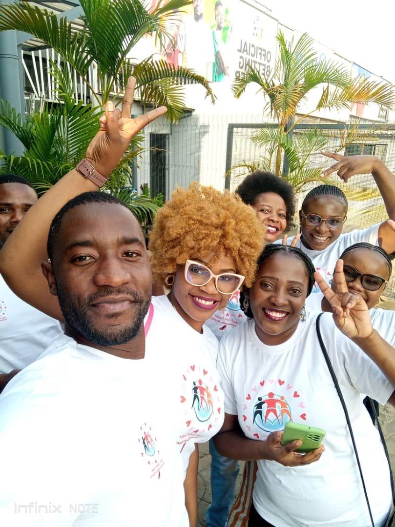 Group of smiling people wearing matching white t-shirts posing outdoors with peace signs.