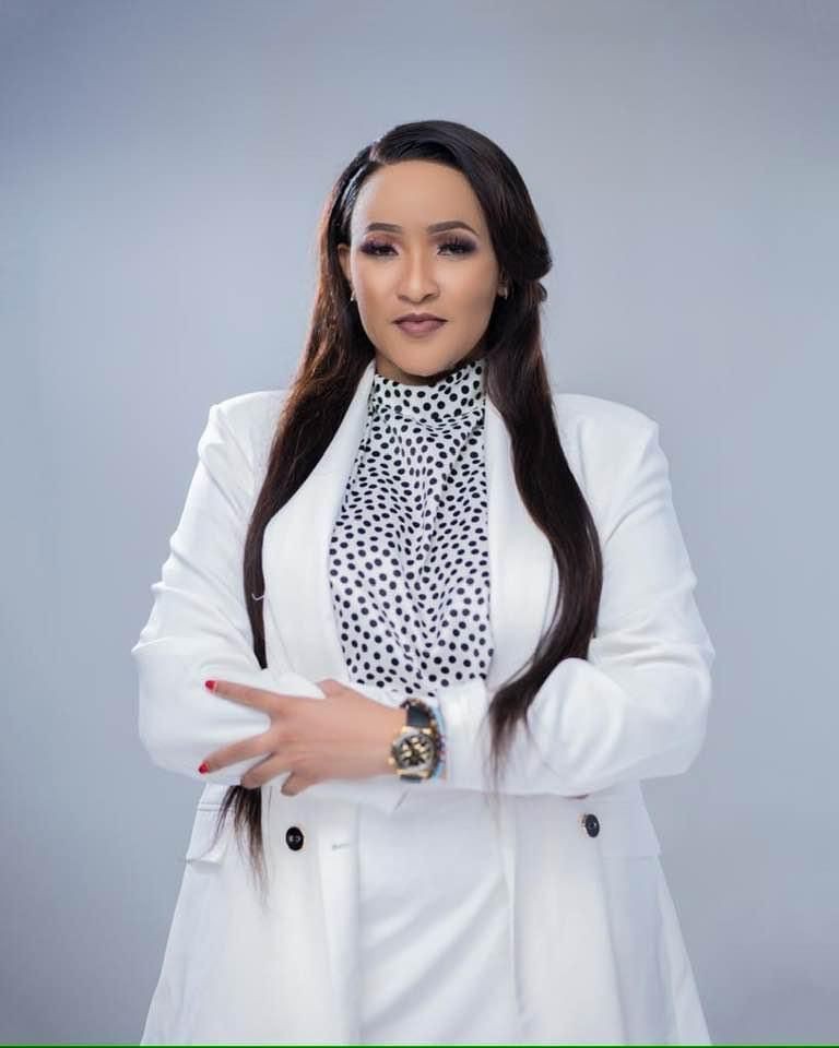 Woman in white suit with long hair posing confidently against a neutral background.
