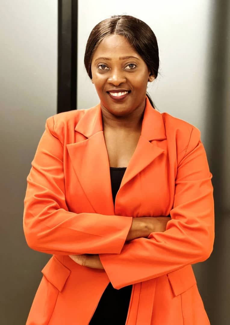 Person wearing an orange blazer with arms crossed in front of a neutral background.