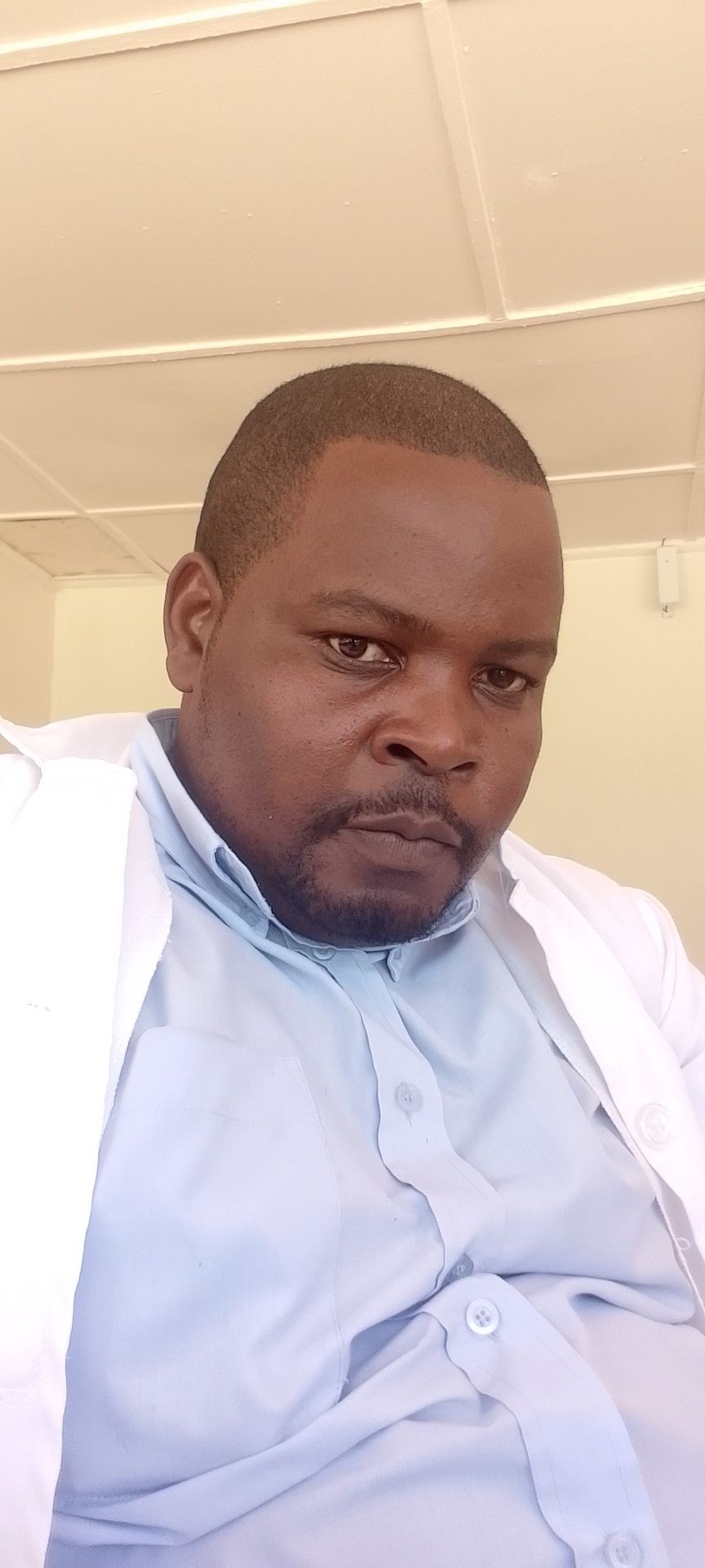 Man in a light blue shirt and white lab coat looking at the camera.