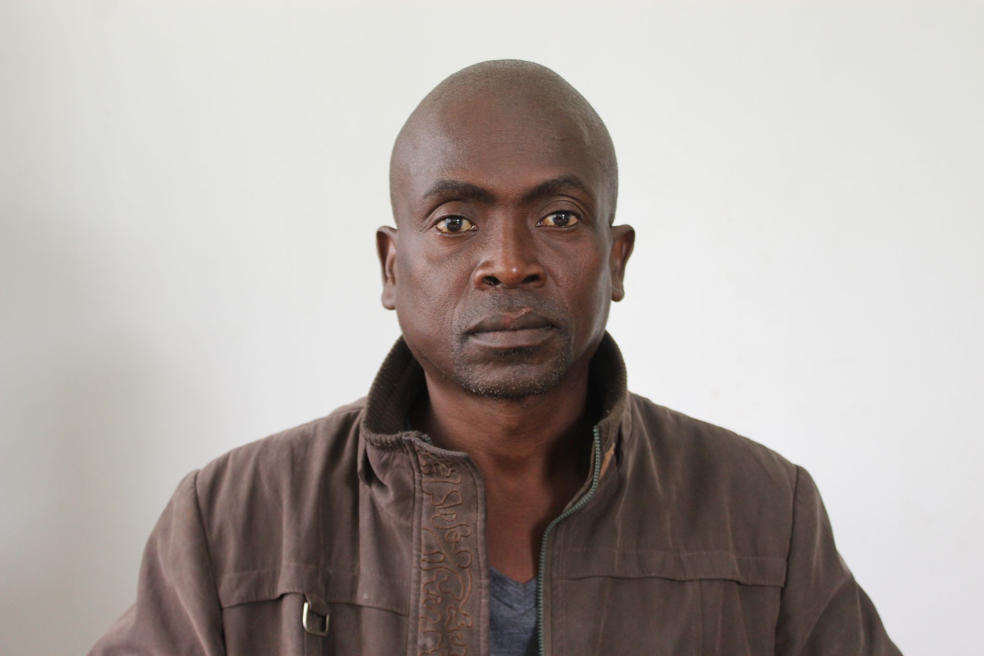 Person wearing a brown jacket with a fur-lined collar, standing against a neutral background.